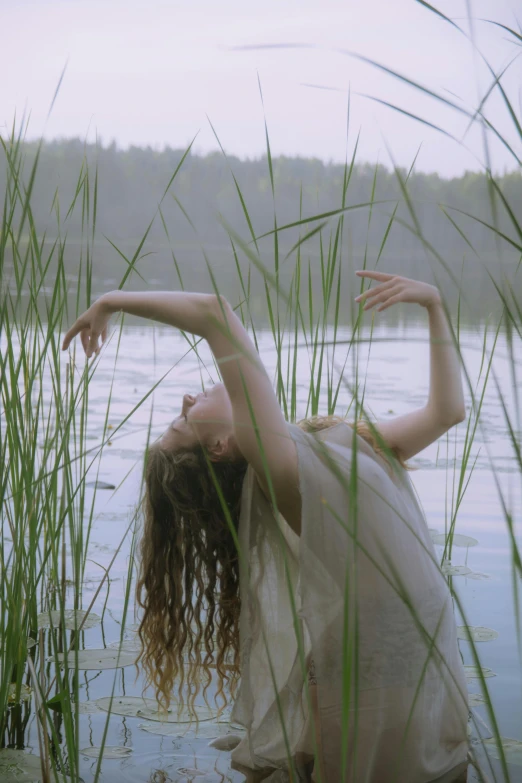 a young woman standing in some tall grass next to the water