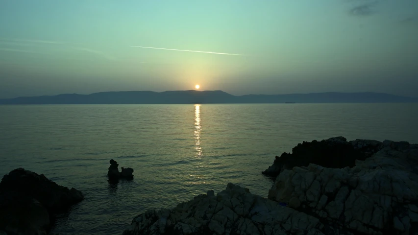 two people are sitting near the ocean watching the sunset