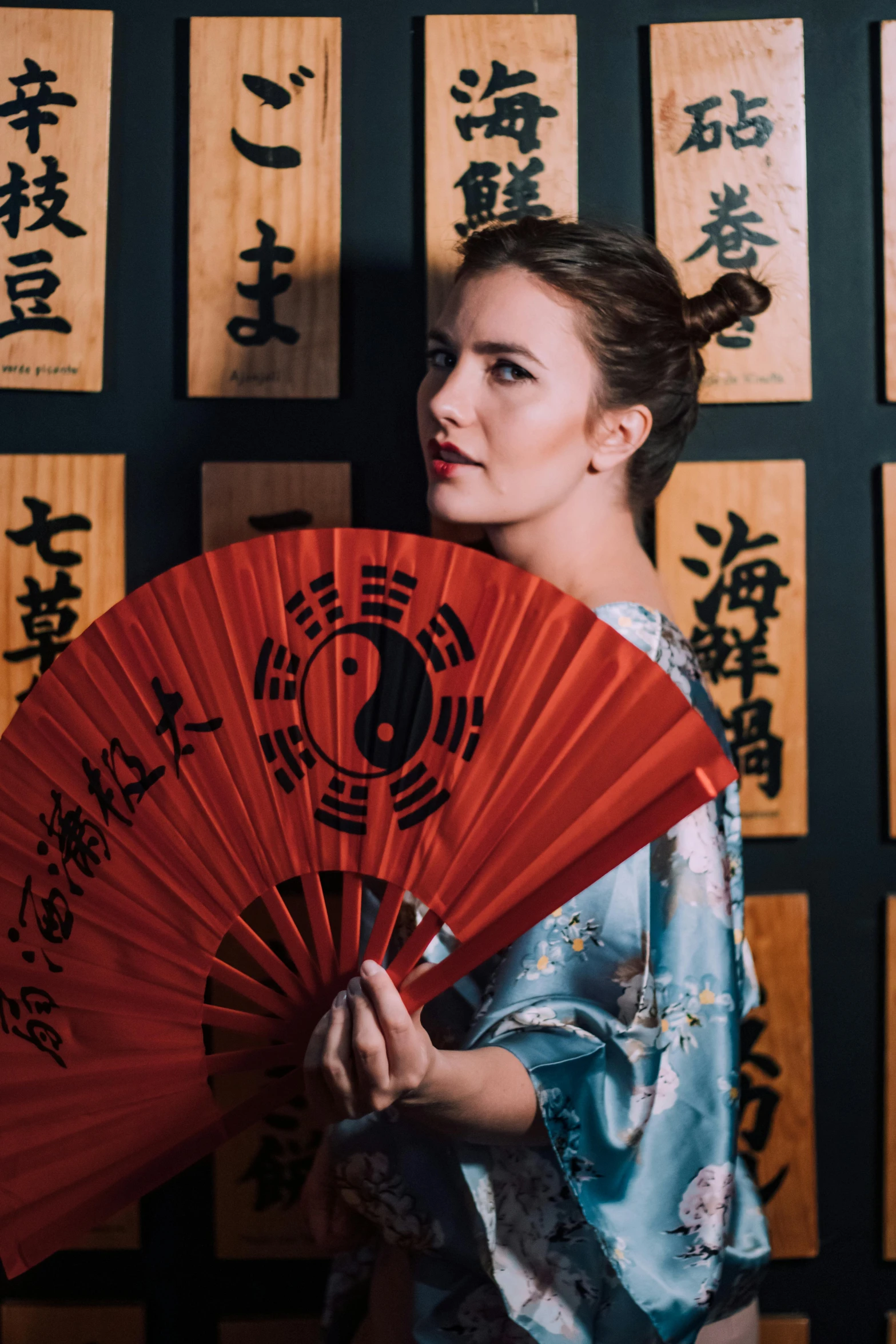 a woman holding an oriental fan and posing in front of a wall with japanese characters