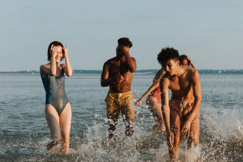 three men and one woman in bathing suit splashing in water near shore