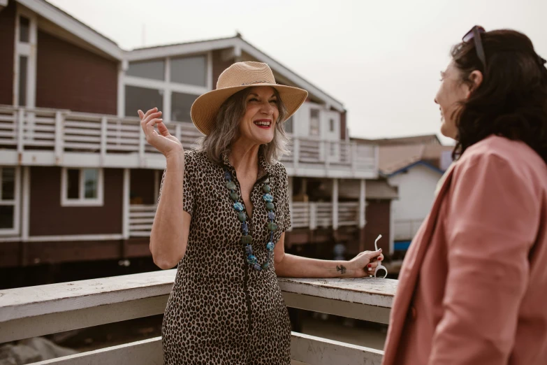 two women on a dock near buildings, one with a hat