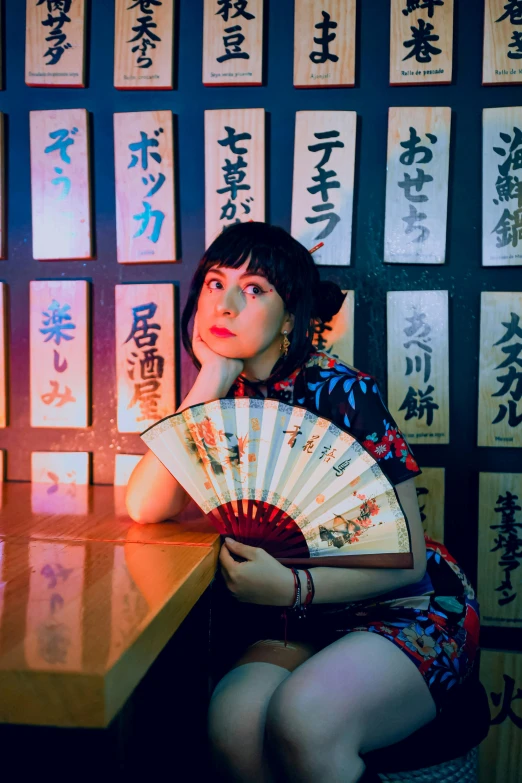 an asian woman holding a fan in front of a wall with writing