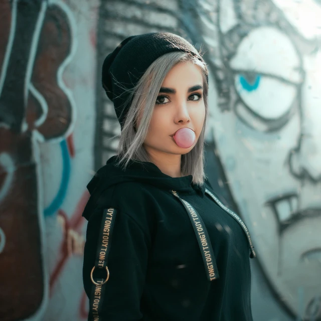 girl blowing bubble with a wall painted with graffiti