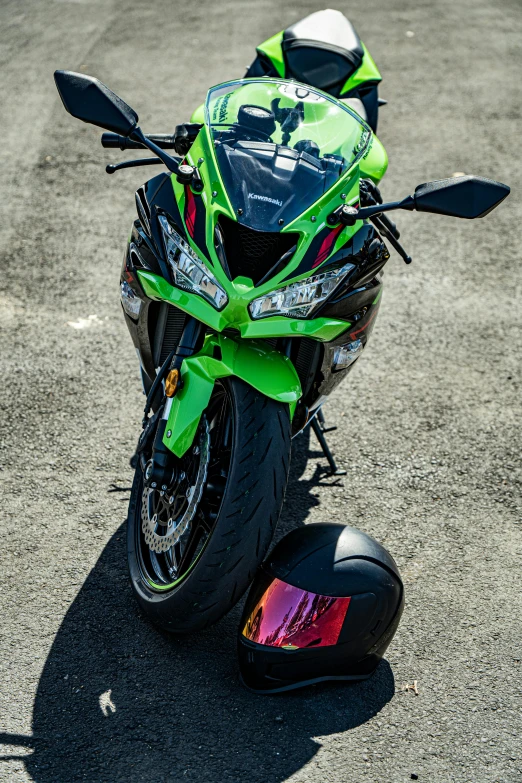 a green motorcycle parked on the asphalt and with a helmet