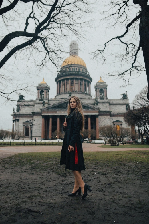 a woman in a black coat standing on the grass outside of a large building