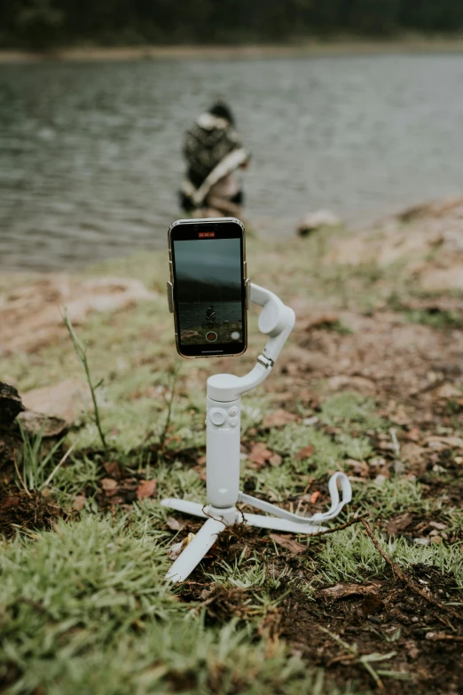 a phone is attached to a holder in the grass near a body of water