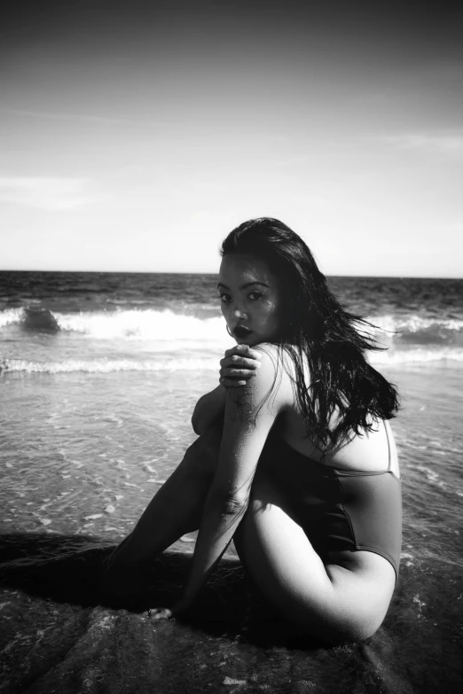 a girl kneeling down on the beach in a bathing suit