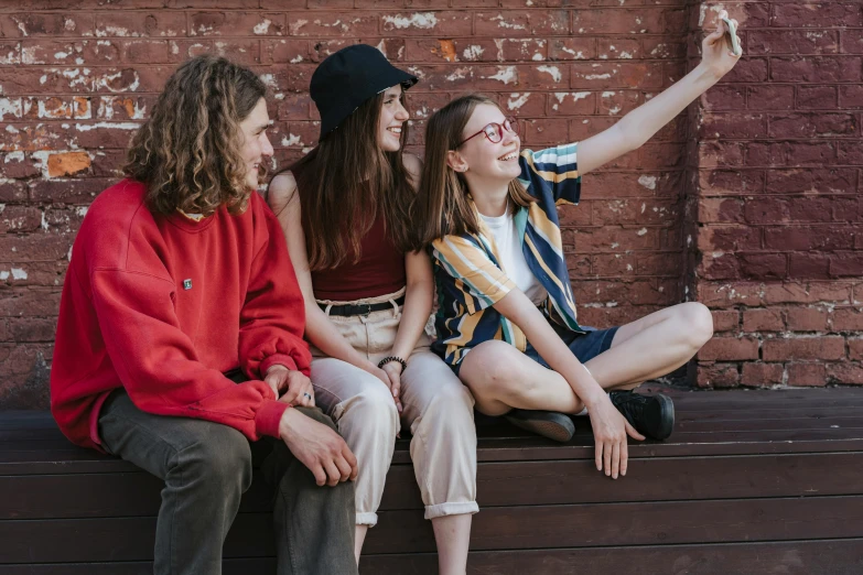 two girls and a man sitting on a bench taking a picture