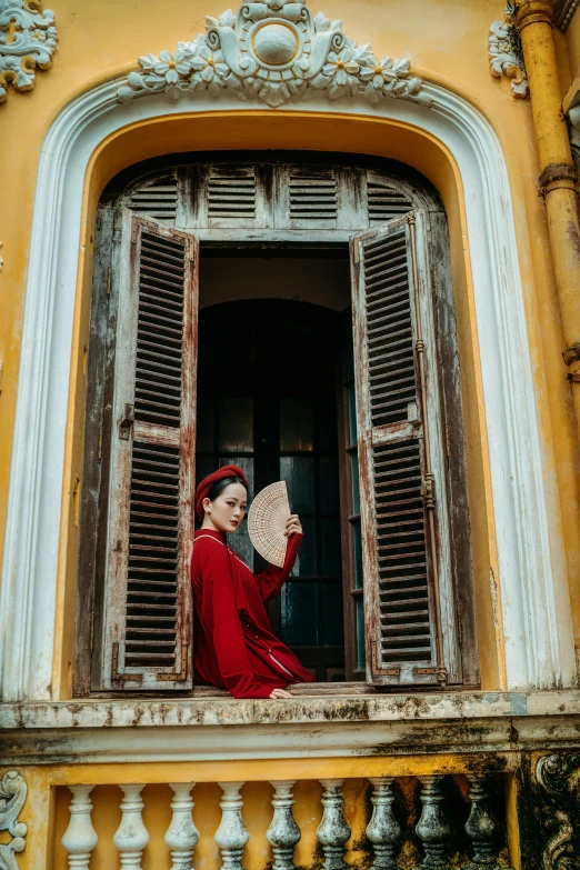 woman with a red scarf and a red hat standing on balcony looking out of window