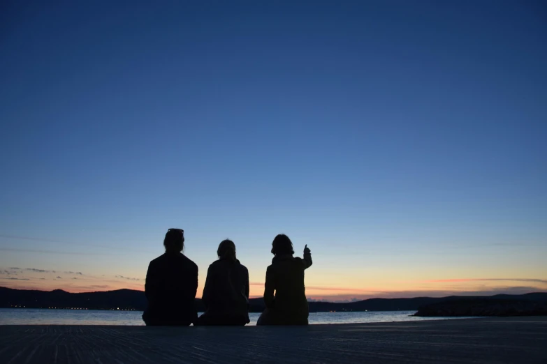 three people sitting on the beach with one looking at soing