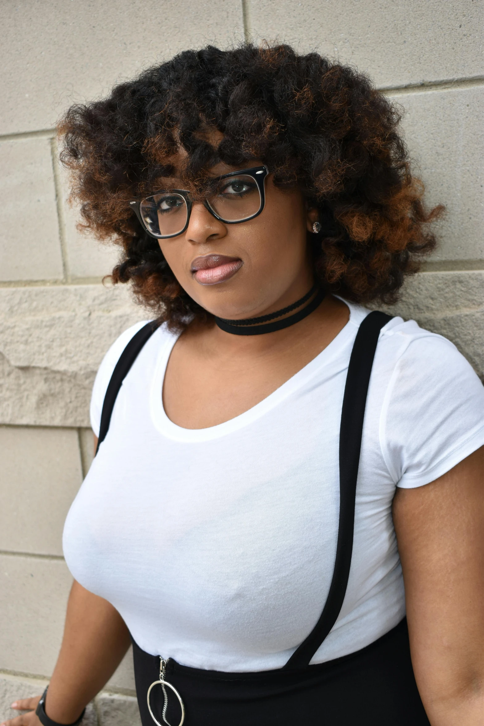 a woman wearing glasses standing against a stone wall