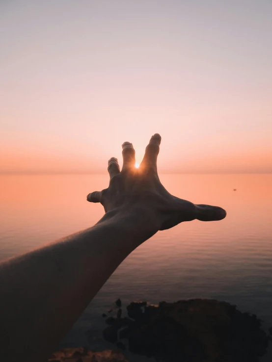 person's hand with one of the fingers reaching for the sun