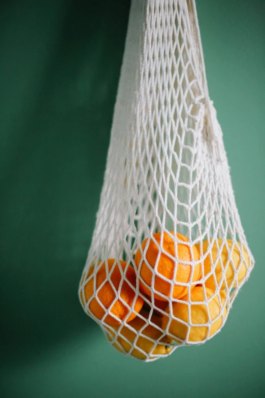 a white mesh bag filled with ripe oranges