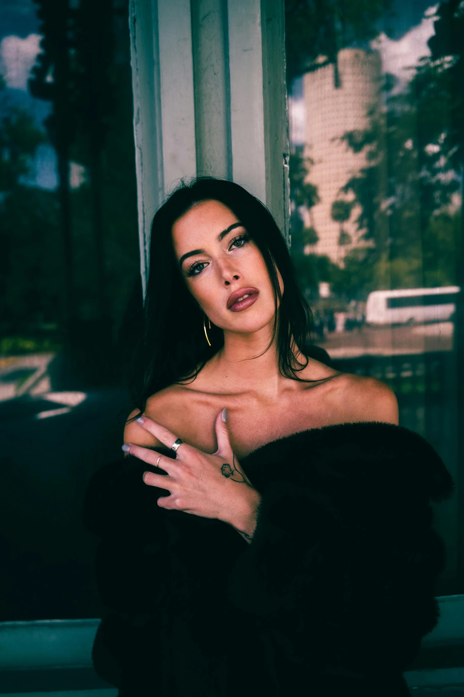 the woman poses in black fur coat in front of a window