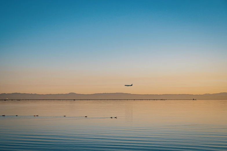 an airplane is flying over the water at sunset