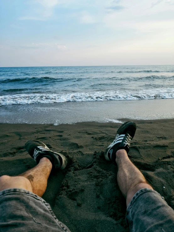 two people sitting on a sandy beach with their feet propped against one another