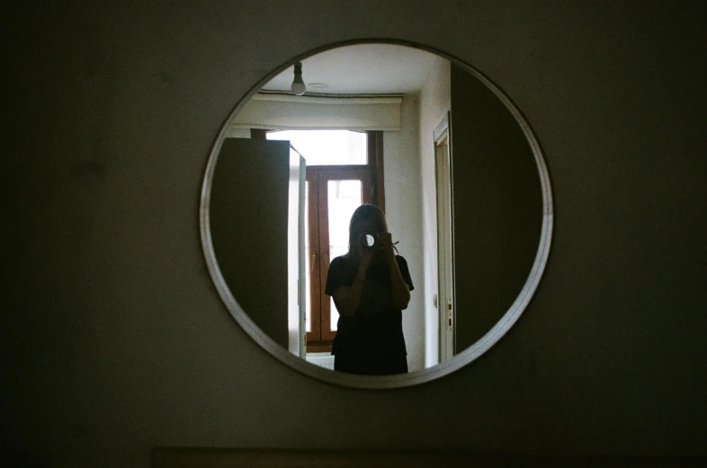 a woman standing behind a door looking through a circular mirror