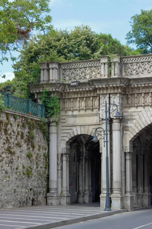 a city sidewalk with an archway covered with vines and columns