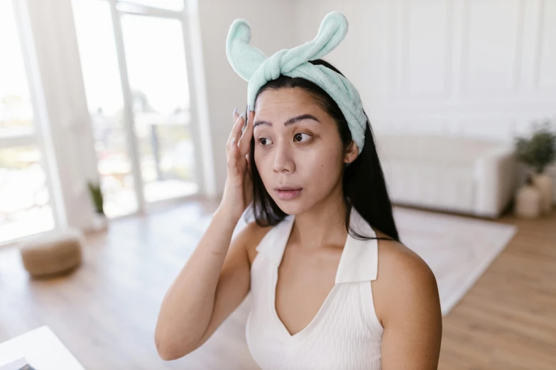 a woman wearing a green bunny ears headband holding her ear