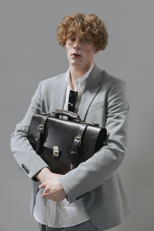 a person in grey jacket and suit holding a leather bag