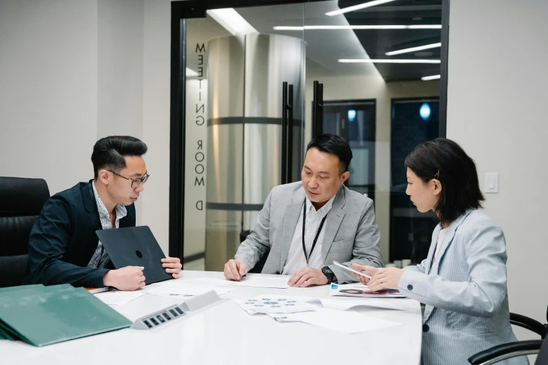 three people are sitting at a table and one person is holding a pen