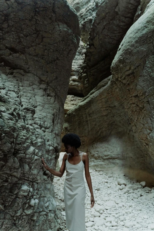 a woman is walking through some rocks wearing a white dress