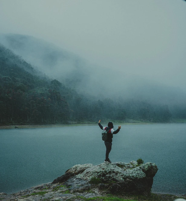 a man standing on top of a large rock near the water