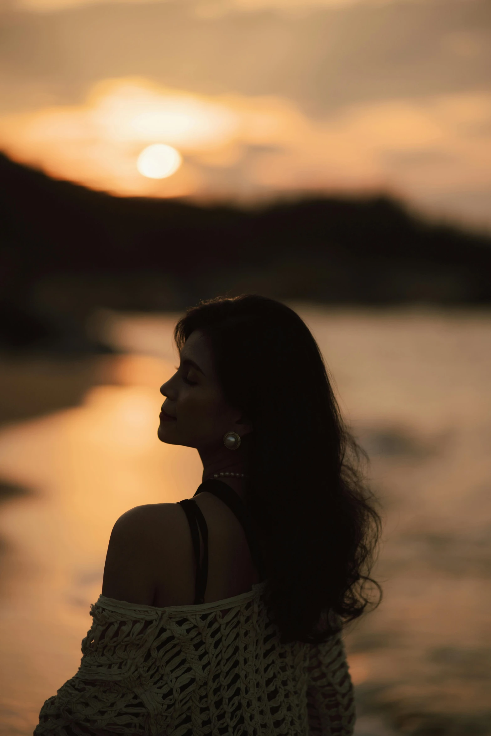 a woman standing by the water in front of a sunset