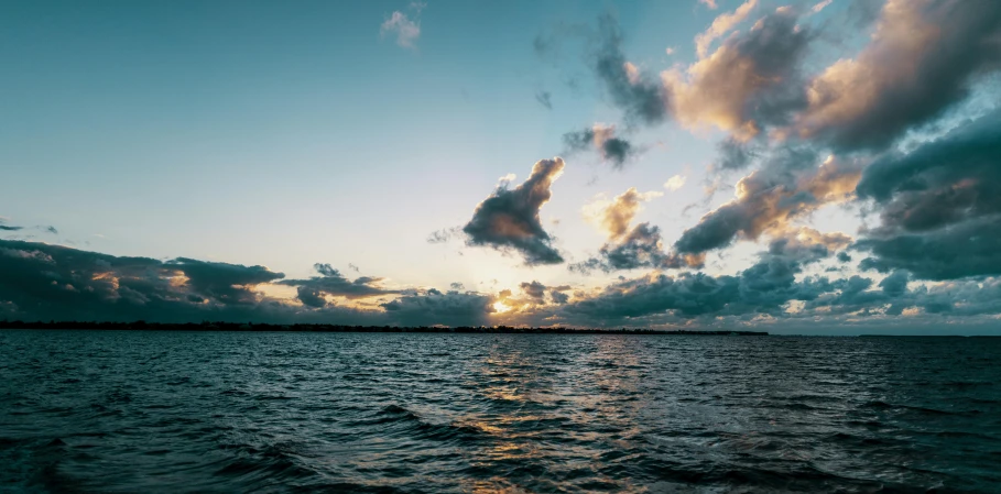 the sunset over a body of water with some clouds in the sky