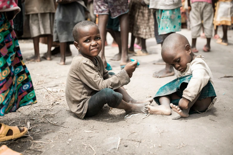 two young children sitting in a dirt field