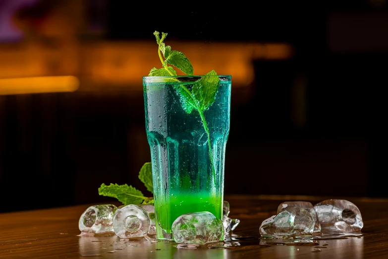 a green drink with ice cubes and mint on a table