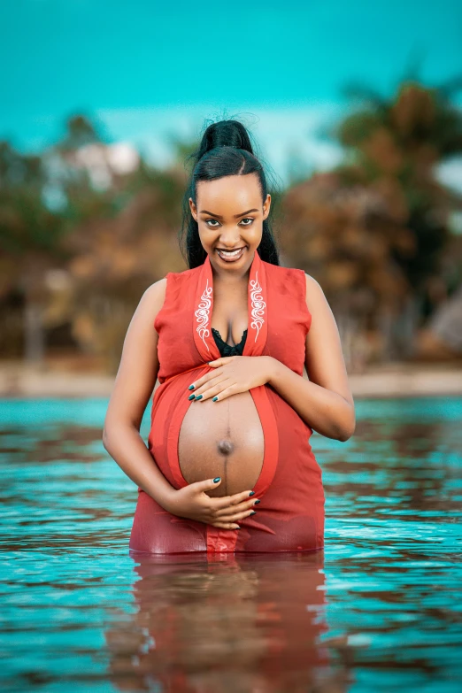 a pregnant woman with her hands on her belly standing in a large body of water