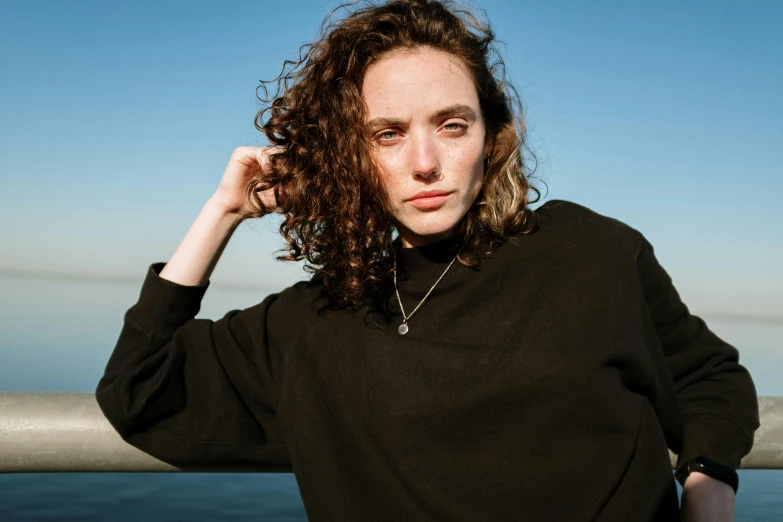 a woman in a black sweater and necklace standing by water