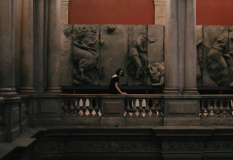 a woman sitting on a balcony in front of some statues