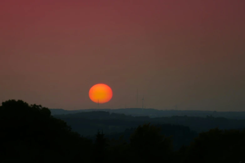 the sun setting over the hills with trees in foreground