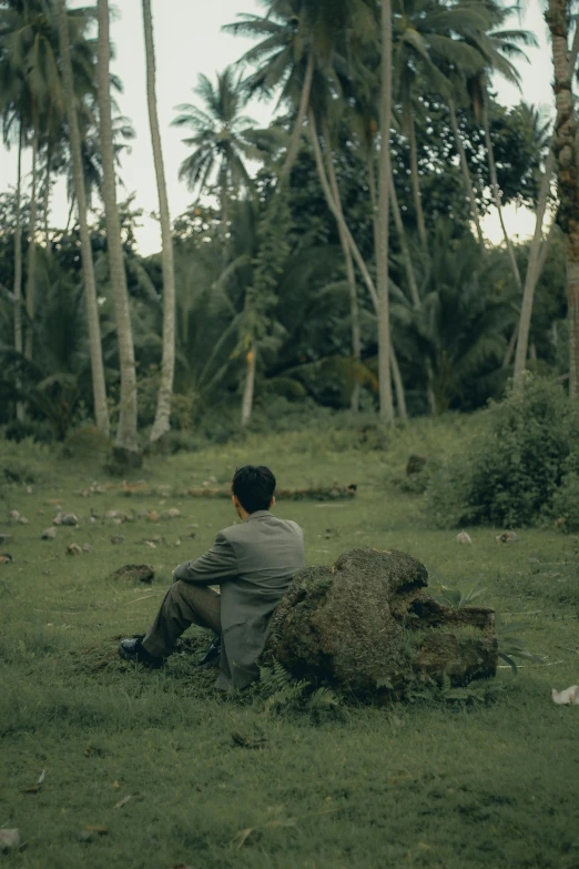 a man sitting in the grass with palm trees behind him