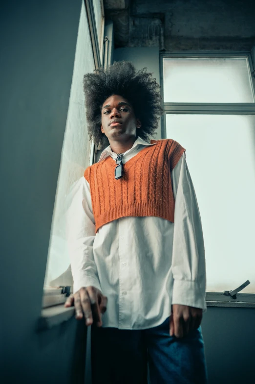 a person wearing an orange sweater vest standing near a window