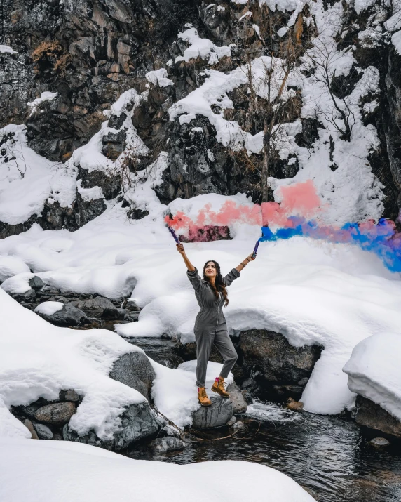 a woman holds up a sign while standing on the edge of a stream of water surrounded by snow