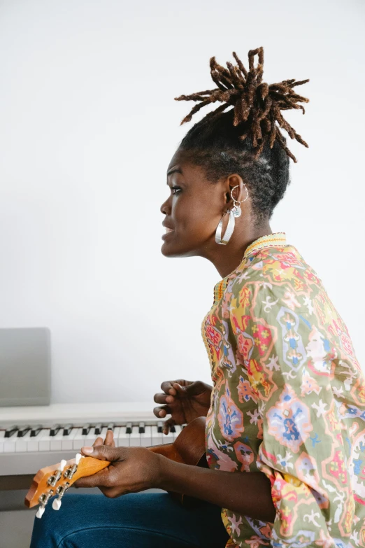a woman sitting at a piano wearing a colorful shirt and earrings