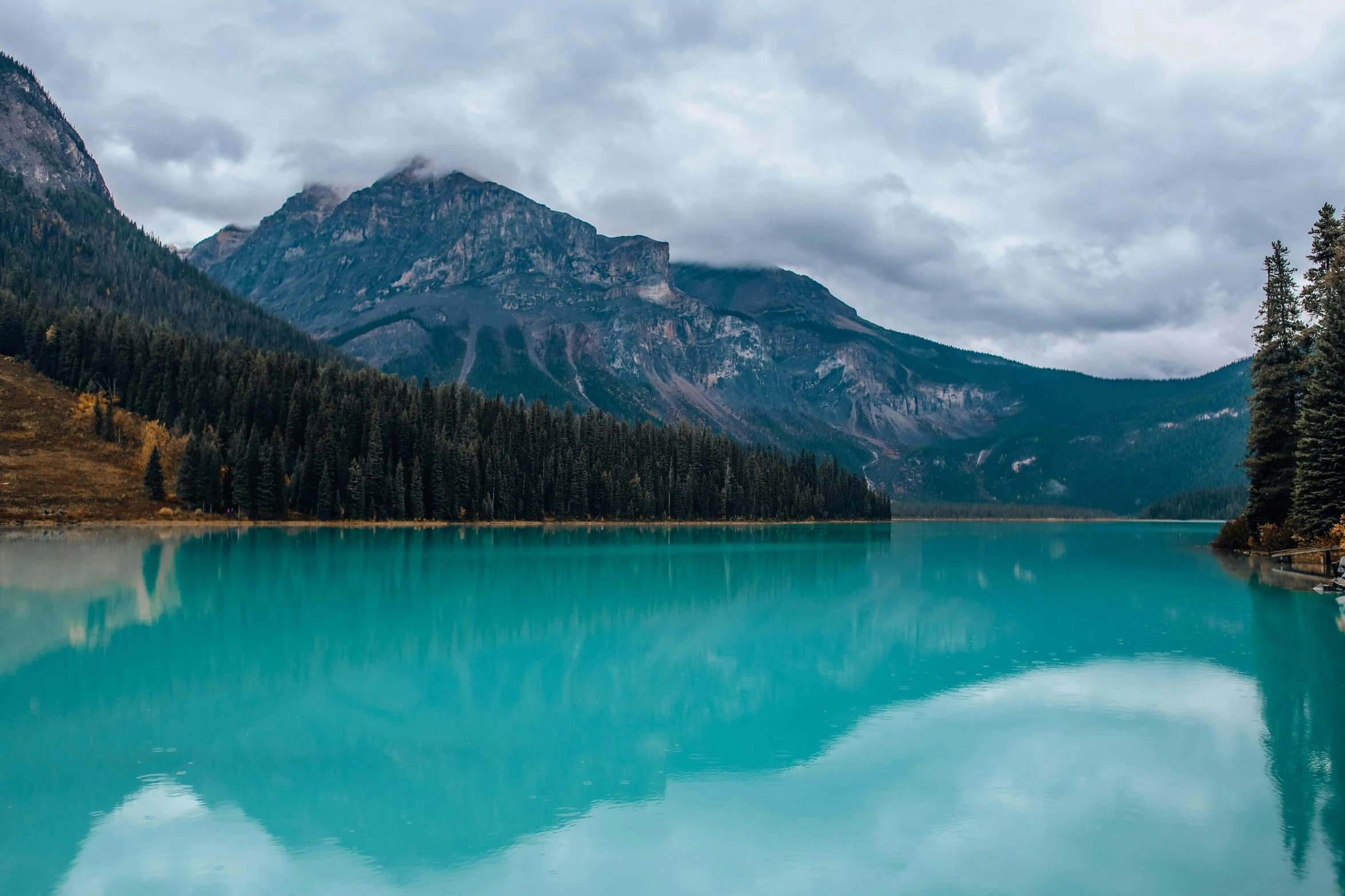 a lake with blue waters near trees on a cloudy day