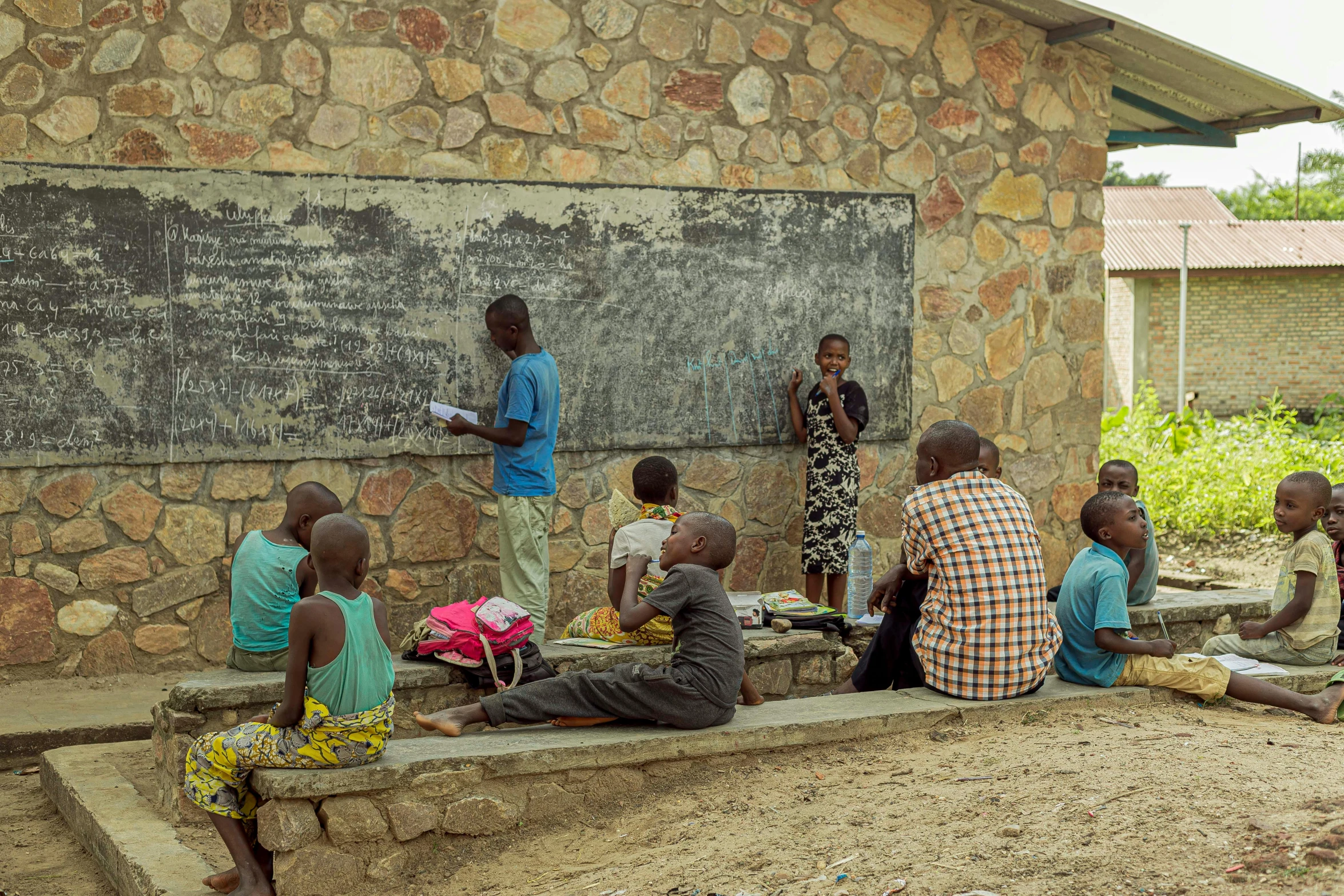 several people sitting on a stone bench looking at chalkboard