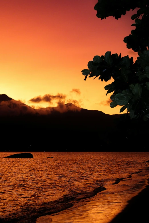 the sun is set at the edge of the water and mountains