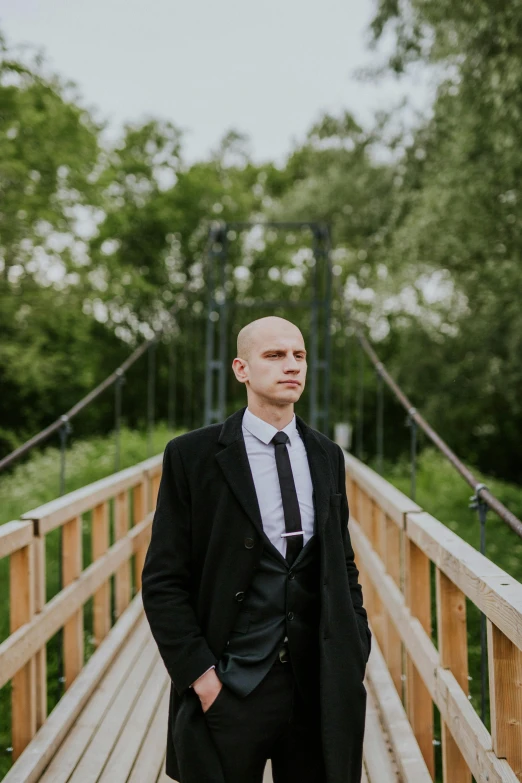 a man wearing a suit and tie standing on a bridge