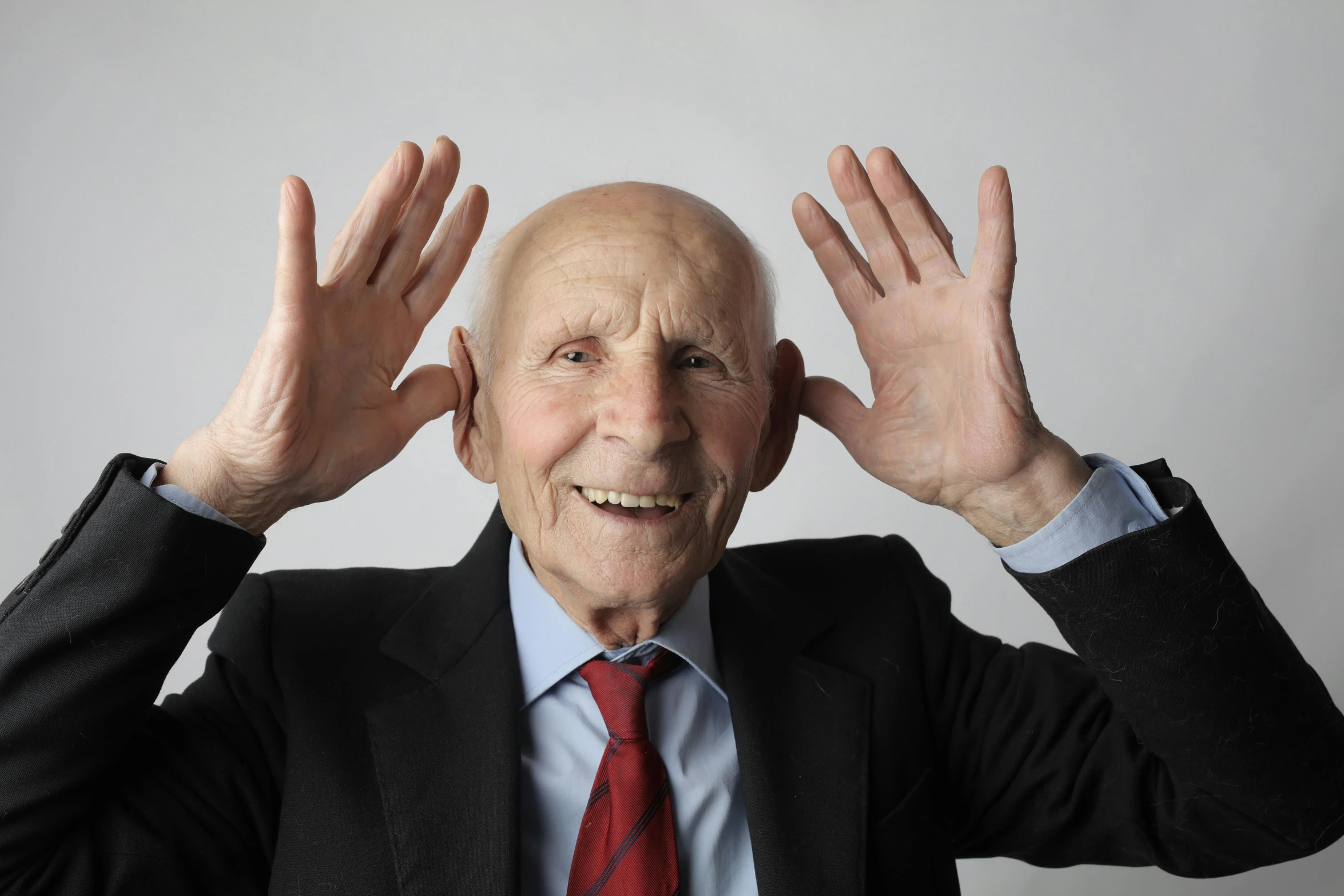 a man is in a suit and red tie covering his ears