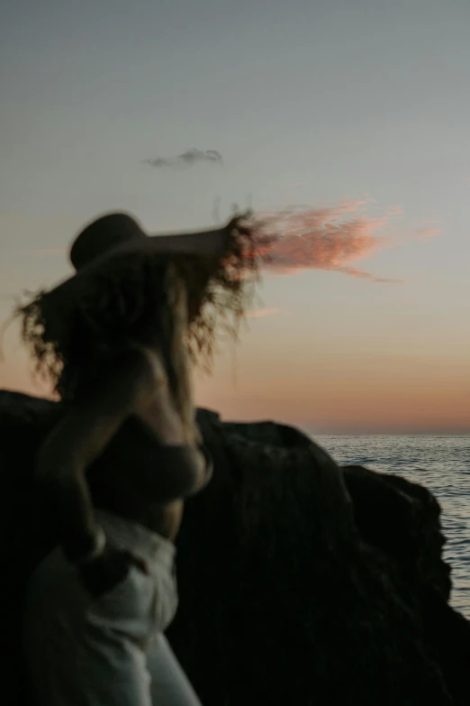 a lady standing on the beach at sunset, watching the ocean and boats sailing by