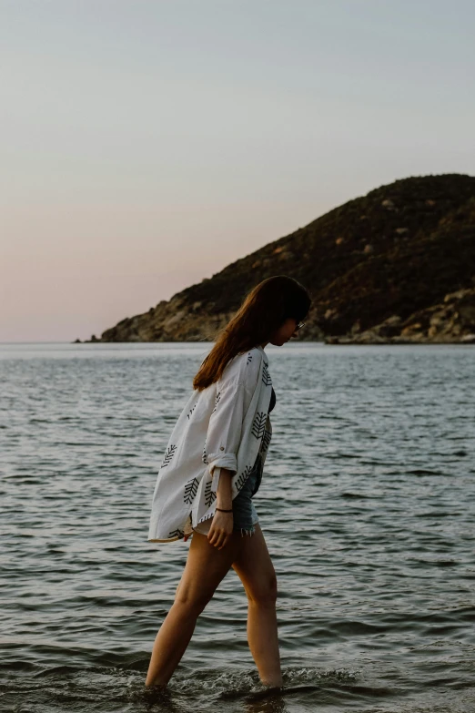 a woman walking in the ocean next to a hill