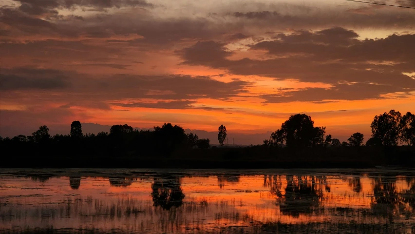 a cloudy sunset over a lake and trees