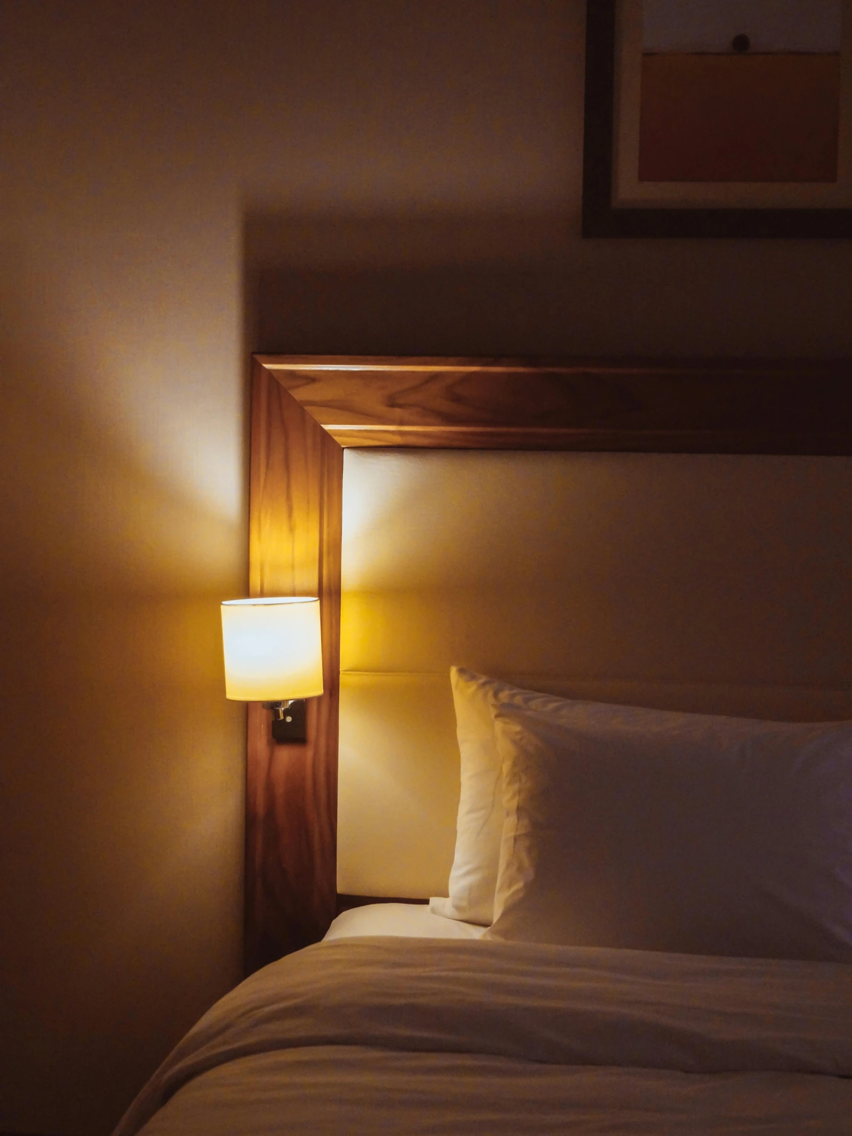 a made bed with white sheets and a small lamps above