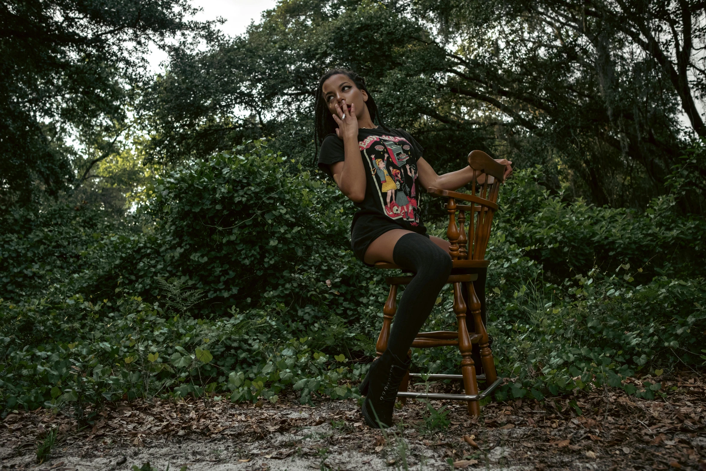 a woman sitting on a wooden chair in a wooded area