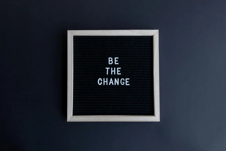 a black wall with a black board that says be the change